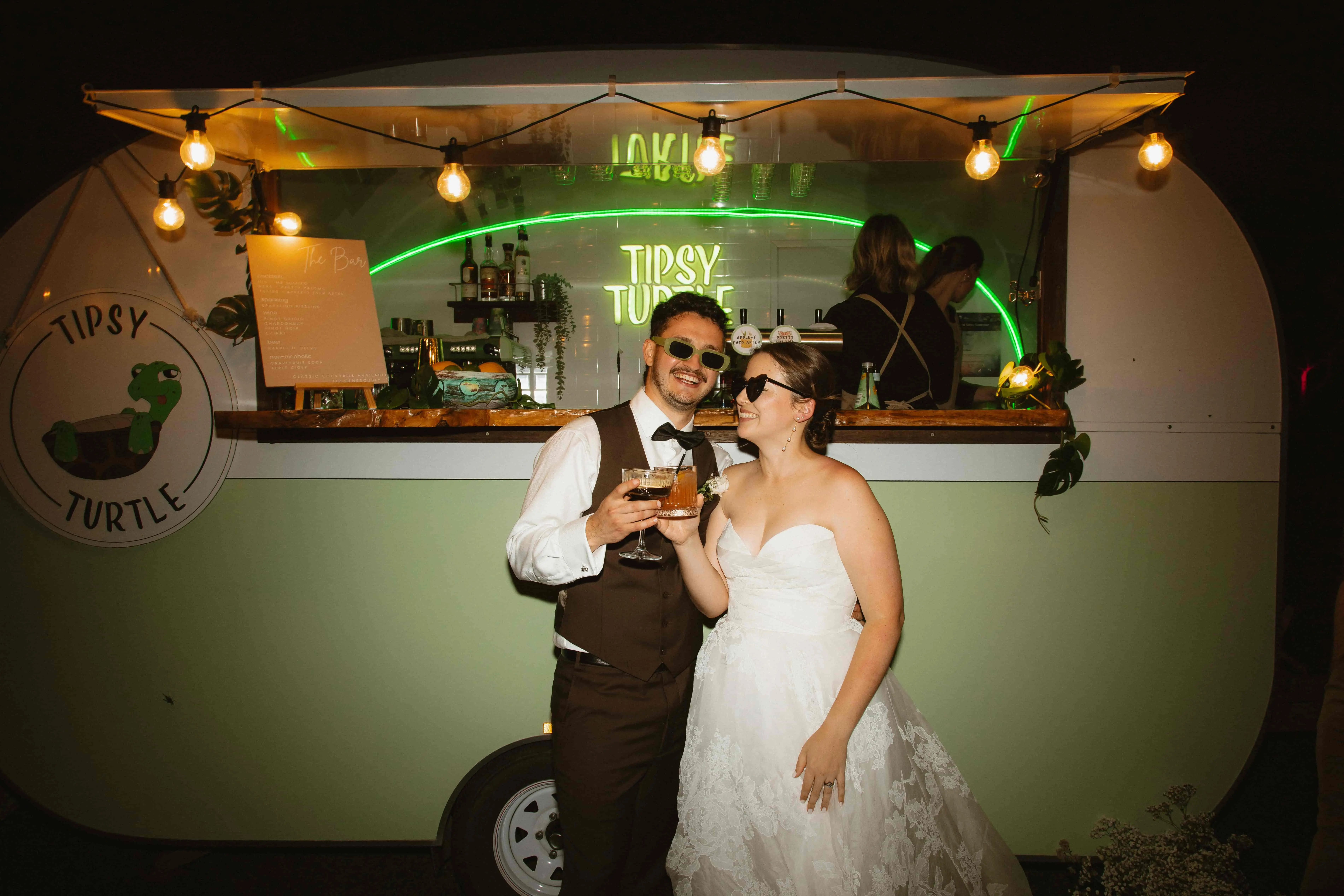 Newlyweds in front of the Tipsy Turtle caravan mobile bar at a Southern Highlands wedding